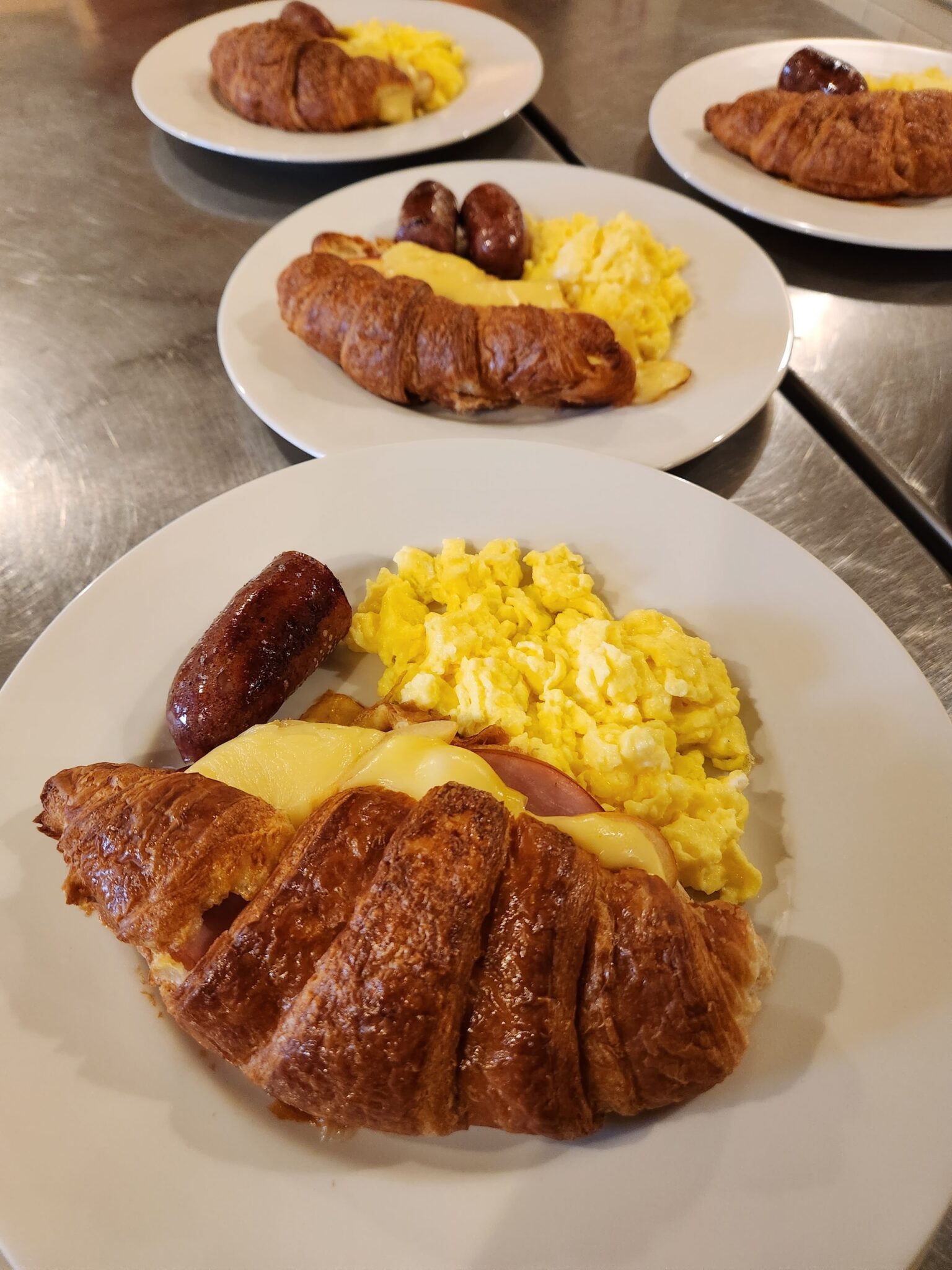 Breakfast of a croissant stuffed with apple, canadian bacon, and gruyere cheese. Accompanied by scrambled eggs and sausage.