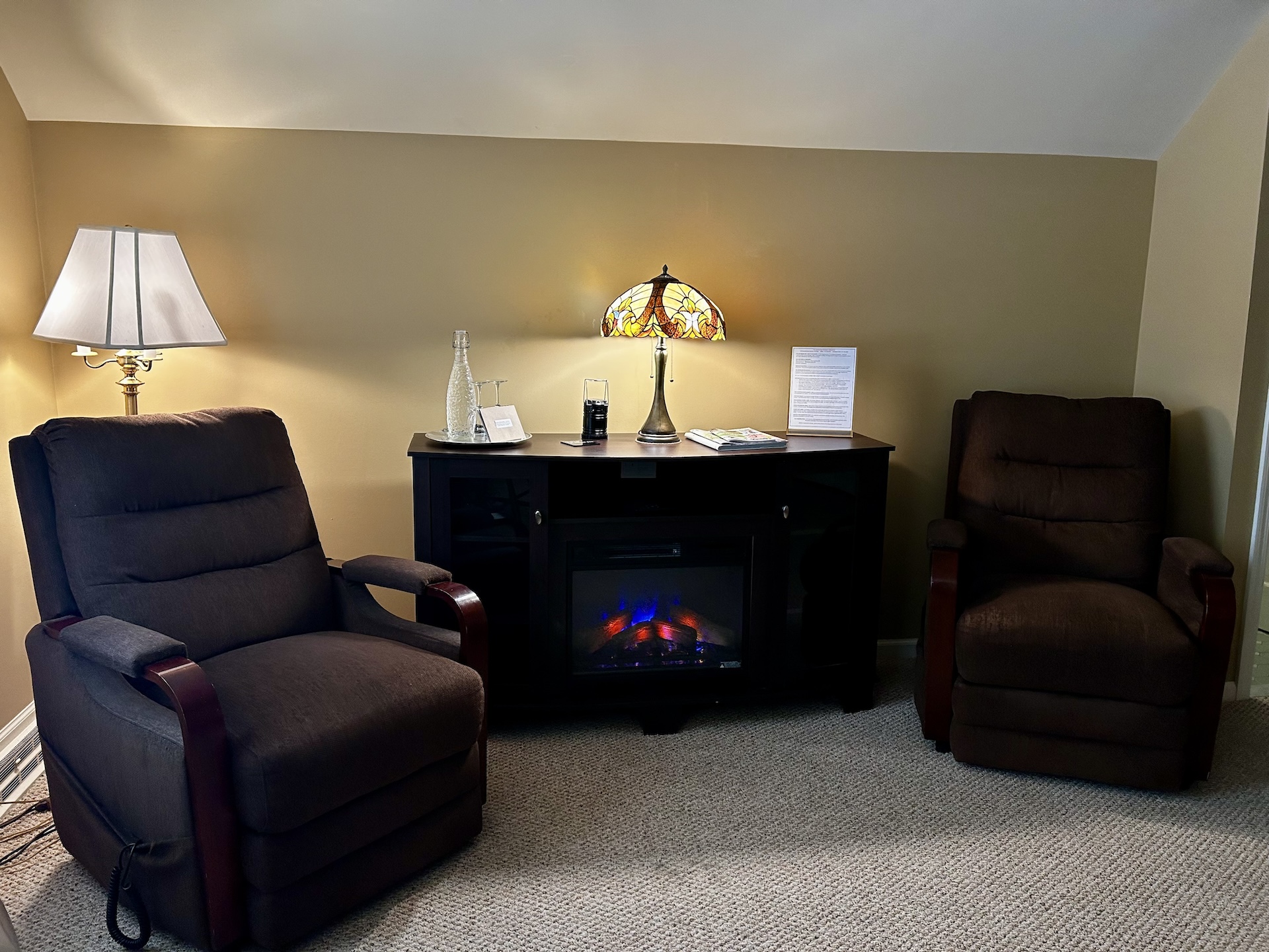 Room 6 Living Area. Two big brown chairs with a table and electric fireplace in between them.